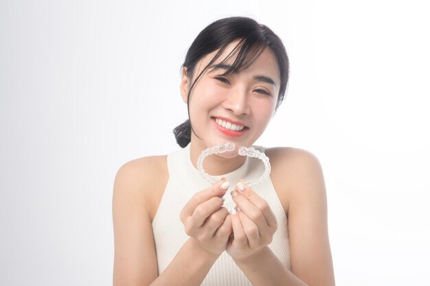 Mulher jovem sorridente segurando aparelho ortopédico invisalign sobre estúdio de fundo branco