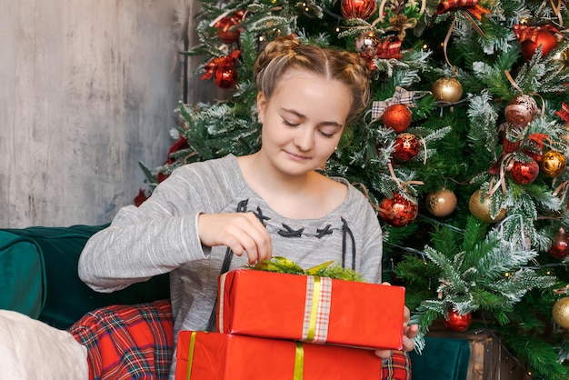 Mulher jovem sorridente segurando caixa de presentes no fundo da árvore de Natal em casa Novo