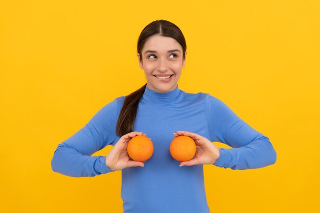 Mulher jovem sorridente segurando frutas cítricas laranja em fundo amarelo, dieta