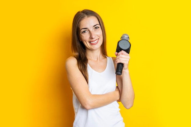 Mulher jovem sorridente segurando um microfone em um fundo amarelo Conceito de repórter ou jornalista