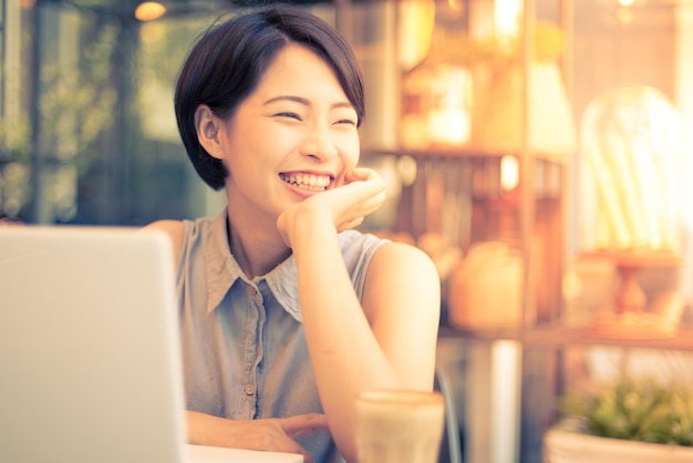Mulher jovem sorridente sentada com café e laptop na mesa em um café