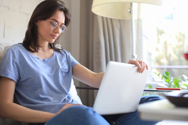 Mulher jovem sorridente sentada no sofá com computador portátil e conversando com amigos