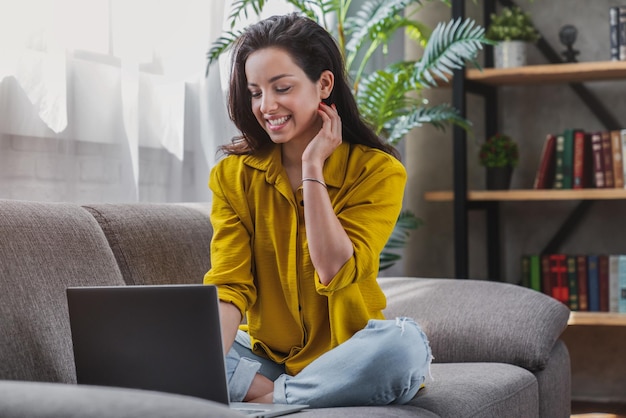 Mulher jovem sorridente sentada no sofá e usando laptop para trabalhar online em casa