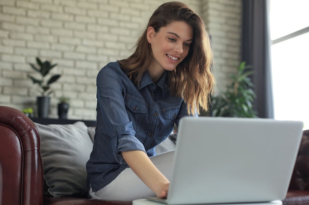 Mulher jovem sorridente, sentado no sofá com o computador portátil e conversando com amigos.