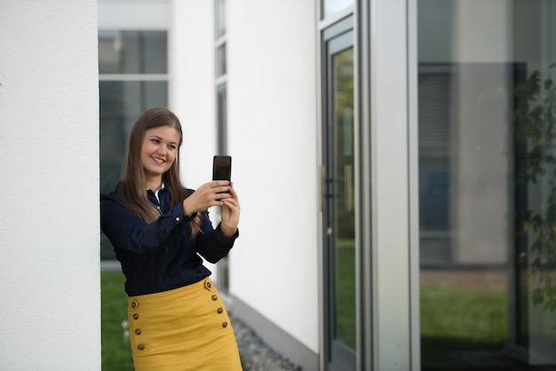 Mulher jovem sorridente tirando selfie através de telefone contra edifícios na cidade