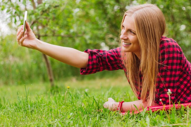 Mulher jovem sorridente tirando selfie com telefone celular no parque