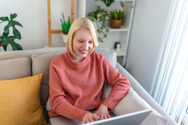 Mulher jovem sorridente usando laptop em casa, olhando para a tela, conversando, usando fone de ouvido sem fio com videoconferência. tutoria de treinador de negócios por webcam, treinamento on-line, conceito de e-coaching