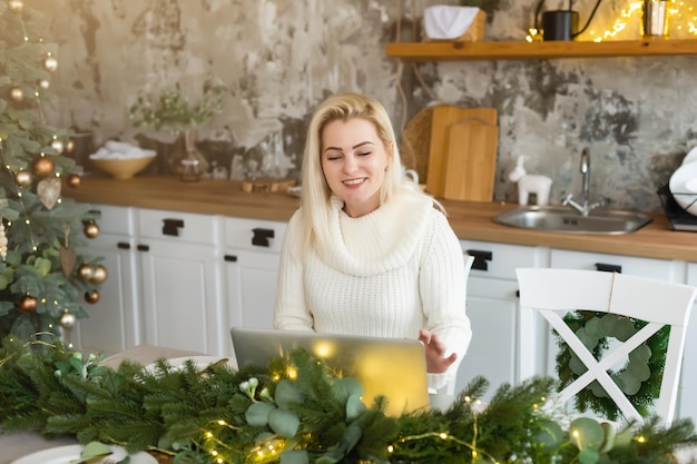 Mulher jovem sorridente usando laptop perto de árvore de natal.