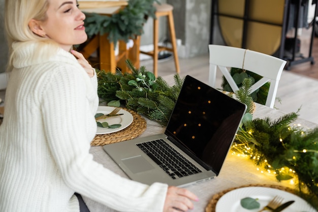 Mulher jovem sorridente usando laptop perto de árvore de natal.