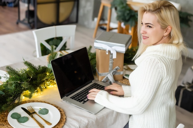 Mulher jovem sorridente usando laptop perto de árvore de natal.