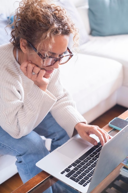 Mulher jovem sorridente usando laptop sentada no sofá em casa garota bonita fazendo compras ou conversando on-line na rede social se divertindo assistindo a filmes freelancer trabalhando em projeto de computador trabalho on-line