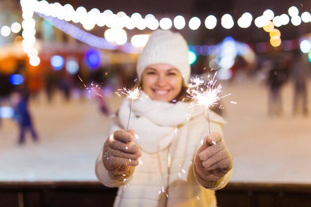 Mulher jovem sorridente usando roupas de malha de inverno segurando diamante ao ar livre sobre um fundo de neve