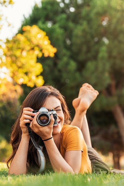 Mulher jovem sorridente usando uma câmera para tirar uma foto no parque.