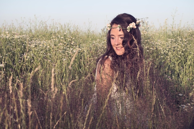 Mulher jovem sorridente vestindo flores enquanto está sentada no meio de plantas