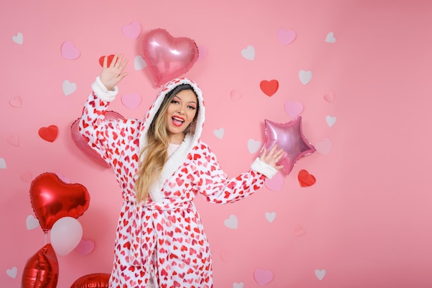 Mulher jovem sorridente vestindo roupão com corações vermelhos Fundo rosa com balões e corações