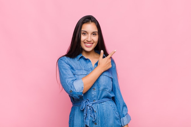 Mulher jovem sorrindo alegremente, sentindo-se feliz e apontando para o lado e para cima, mostrando o objeto no espaço da cópia