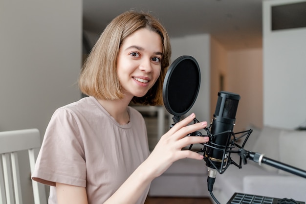 Mulher jovem sorrindo e cantando no microfone no home studio