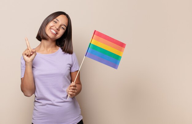 Mulher jovem sorrindo e parecendo amigável, mostrando o número um ou primeiro com a mão para a frente, em contagem regressiva