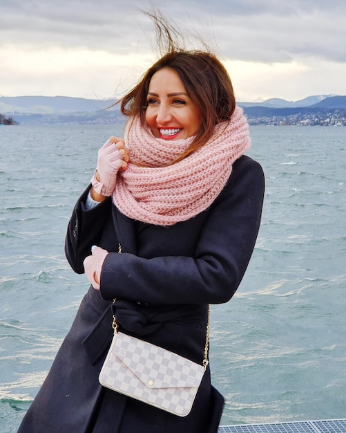 Foto mulher jovem sorrindo enquanto está de pé na costa do mar