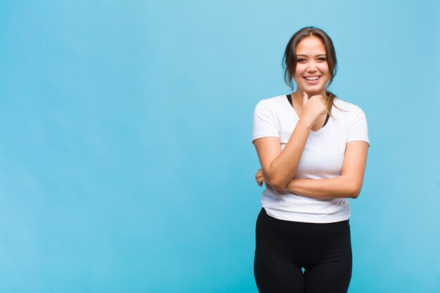 Mulher jovem sorrindo, feliz, amigável, satisfeita e despreocupada com a mão no queixo