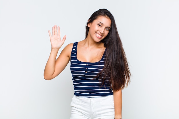 Mulher jovem sorrindo feliz e alegre, acenando com a mão, dando as boas-vindas e cumprimentando você ou dizendo adeus