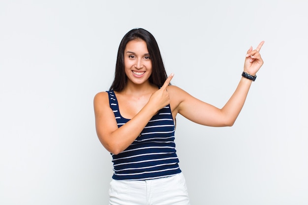 Mulher jovem sorrindo feliz e apontando para o lado e para cima com as duas mãos mostrando o objeto no espaço da cópia