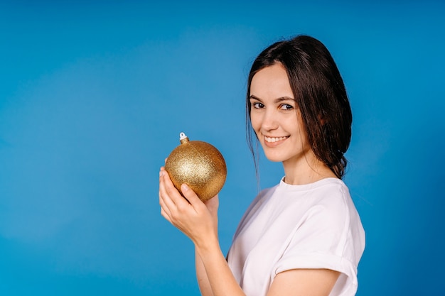 Mulher jovem sorriso com brinquedo de Natal na mão, isolado na parede azul.