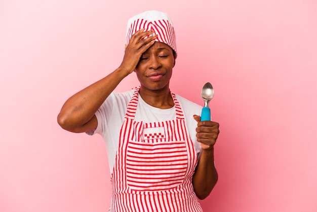 Mulher jovem sorveteira afro-americana segurando a colher isolada no fundo rosa sendo chocada, ela se lembrou de uma reunião importante.