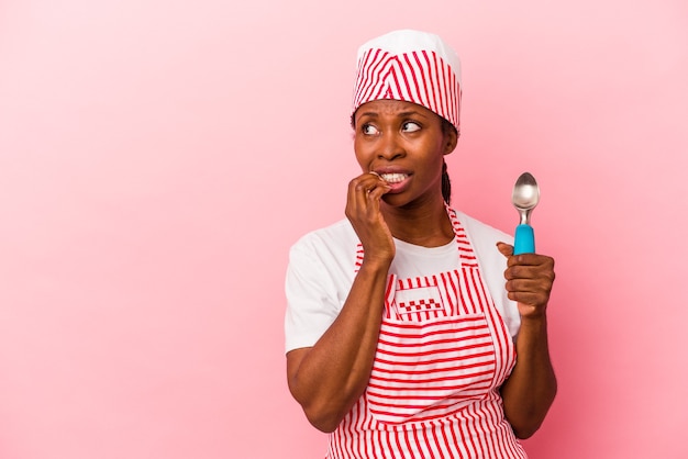 Mulher jovem sorveteira afro-americana segurando colher isolada no fundo rosa relaxada pensando em algo olhando para um espaço de cópia.