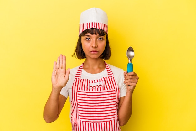 Foto mulher jovem sorveteira de raça mista segurando uma colher de sorvete isolada em fundo amarelo