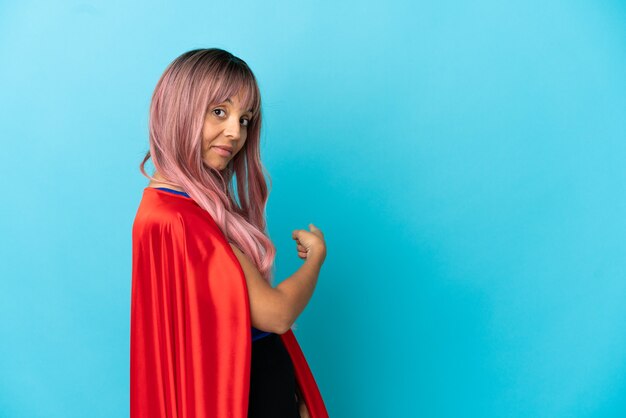 Mulher jovem super-heroína com cabelo rosa isolado em um fundo azul apontando para trás