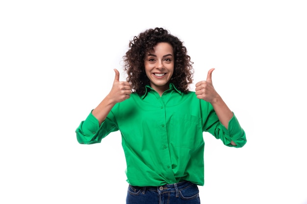 Mulher jovem surpreendida com cabelos ondulados pretos vestida com uma blusa verde aponta os dedos para cima