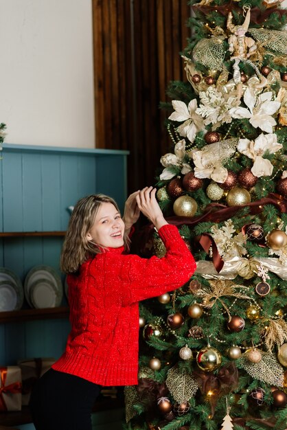 Mulher jovem surpresa emocional feliz por uma árvore de natal na aconchegante sala de estar, o conceito de felicidade