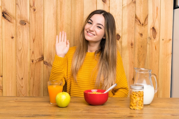 Mulher jovem, tendo, pequeno almoço, em, um, cozinha, saudando, com, mão, com, feliz, expressão