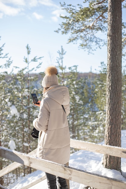Mulher jovem tira uma foto com o celular em um bosque nevado