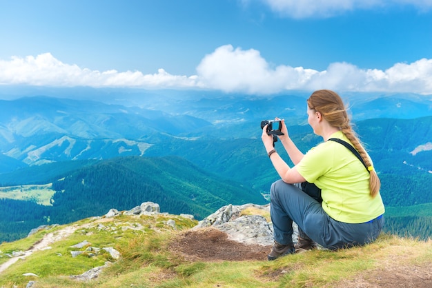 Mulher jovem tirando foto de viagem para a câmera na falésia da montanha