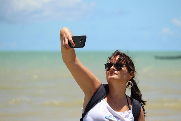 Foto mulher jovem tirando selfie na praia contra o céu