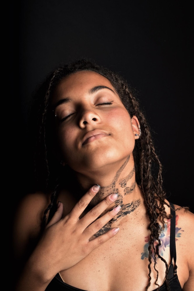 Foto mulher jovem tocando o pescoço enquanto está de pé contra um fundo preto