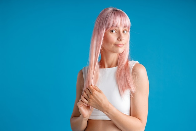 Mulher jovem tocando seu cabelo liso natural longo tingido de rosa e parecendo surpresa posando isolada