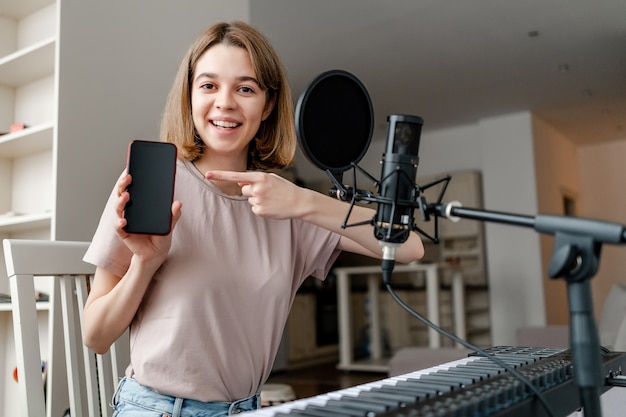 Mulher jovem tocando sintetizador, cantando cover e apontando no aplicativo móvel