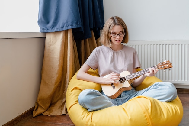 Mulher jovem tocando ukulele em casa