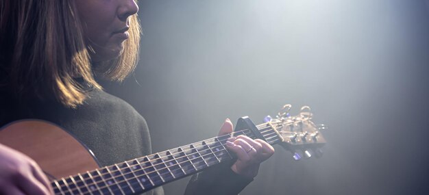 Mulher jovem tocando violão em um quarto escuro com neblina