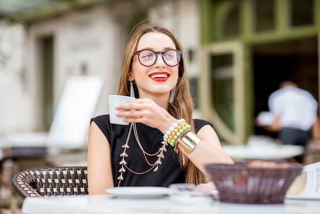 Mulher jovem tomando café da manhã com café e croissant sentada ao ar livre no típico terraço de um café francês durante a manhã na França