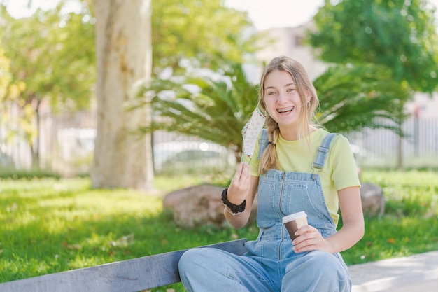 Mulher jovem tomando café e rindo no parque durante a pandemia