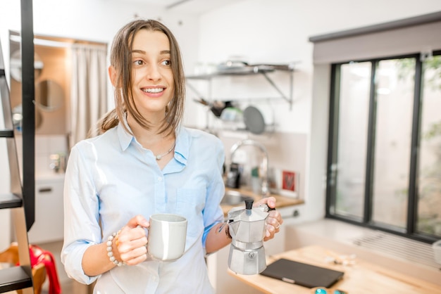 Mulher jovem tomando café em pé na pequena cozinha da casa de campo