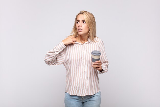 Mulher jovem tomando um café sentindo-se estressada, ansiosa, cansada e frustrada, puxando a gola da camisa, parecendo frustrada com o problema