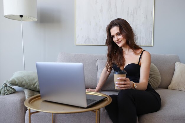 Mulher jovem trabalhando em casa em um laptop e bebendo café