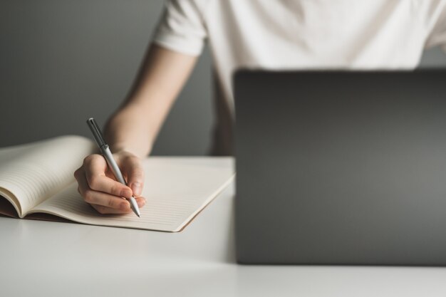 Mulher jovem trabalhando em um laptop e fazendo anotações em um caderno