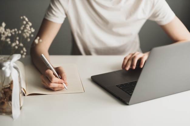 Mulher jovem trabalhando em um laptop e fazendo anotações em um caderno