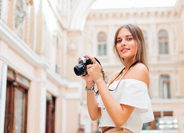 Mulher jovem turista com uma câmera retro nas mãos enquanto posava em arquitetura antiga urbana. Descubra novos lugares